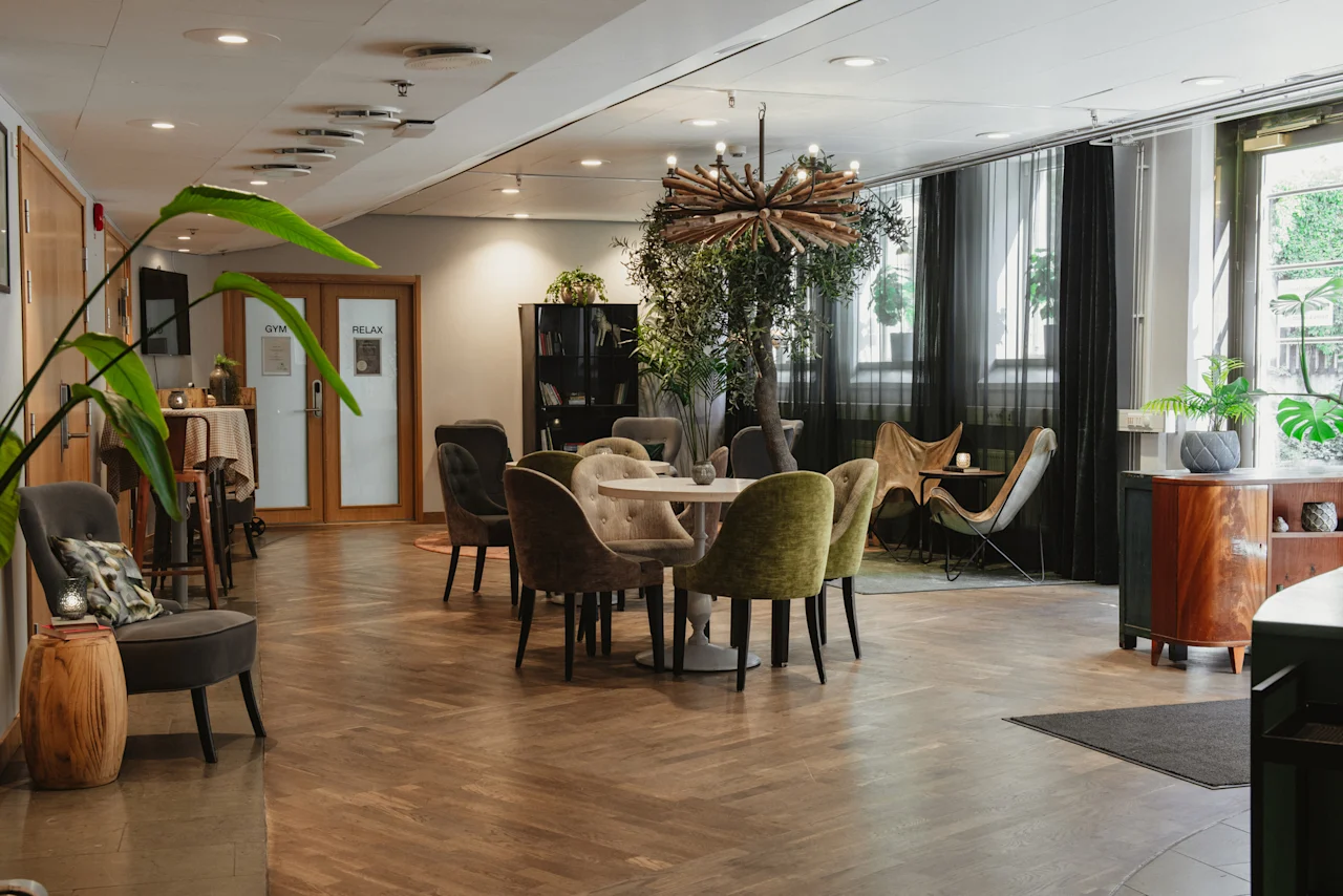 A cozy lounge area at Home Hotel Uppsala with various seating, plants, and doors labeled GYM and RELAX.