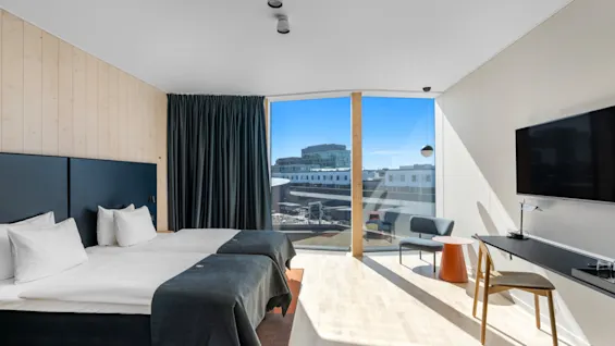 Et lyst, moderne hotelværelse med to enkeltsenge, et stort vindue med udsigt over byen og et behageligt siddeområde.