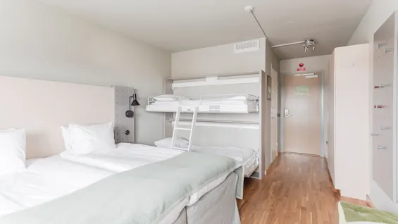 A bright hotel room with a large bed and a bunk bed above, offering comfortable accommodation for families or groups.