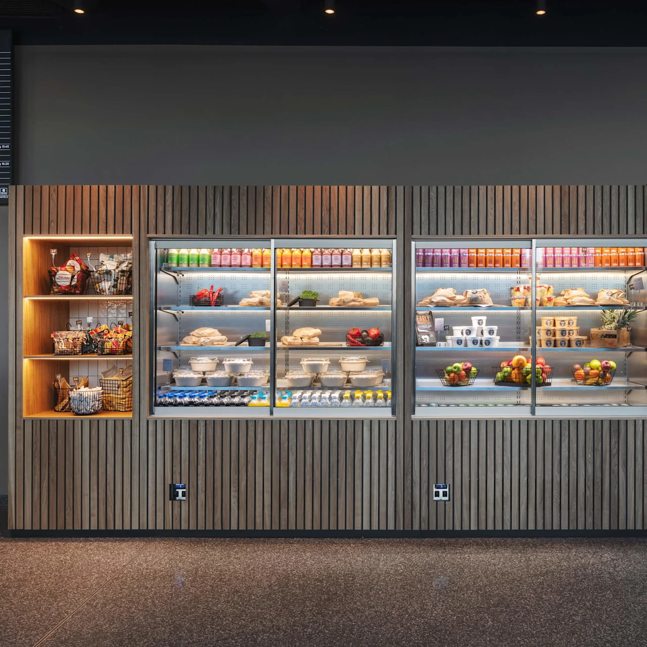 Deli stocked with beverages and food in hotel lobby, with a flight information display in the background.