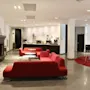 Red sofas encircle round tables in a spacious, modern lobby. A fireplace and coffee station add comfort, while high stools and tables sit on a circular red rug nearby.