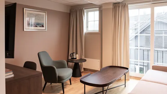 A cozy and inviting hotel room with comfortable seating, a coffee table, and large windows letting in natural light.