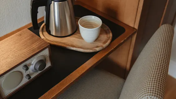 En elkedel og kop på en træbakke, ved siden af en radio, klar til en varm drik og lidt musik i hyggelige omgivelser.