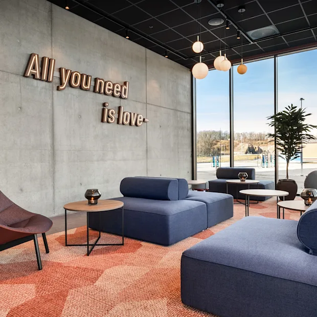 Et moderne og innbydende loungeområde med blå sofaer, mønstret teppe og betongvegg med teksten 'All you need is love'.