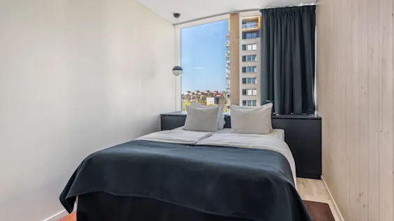 Et moderne hotelværelse med en komfortabel seng og et stort vindue, der tilbyder udsigt over byen.