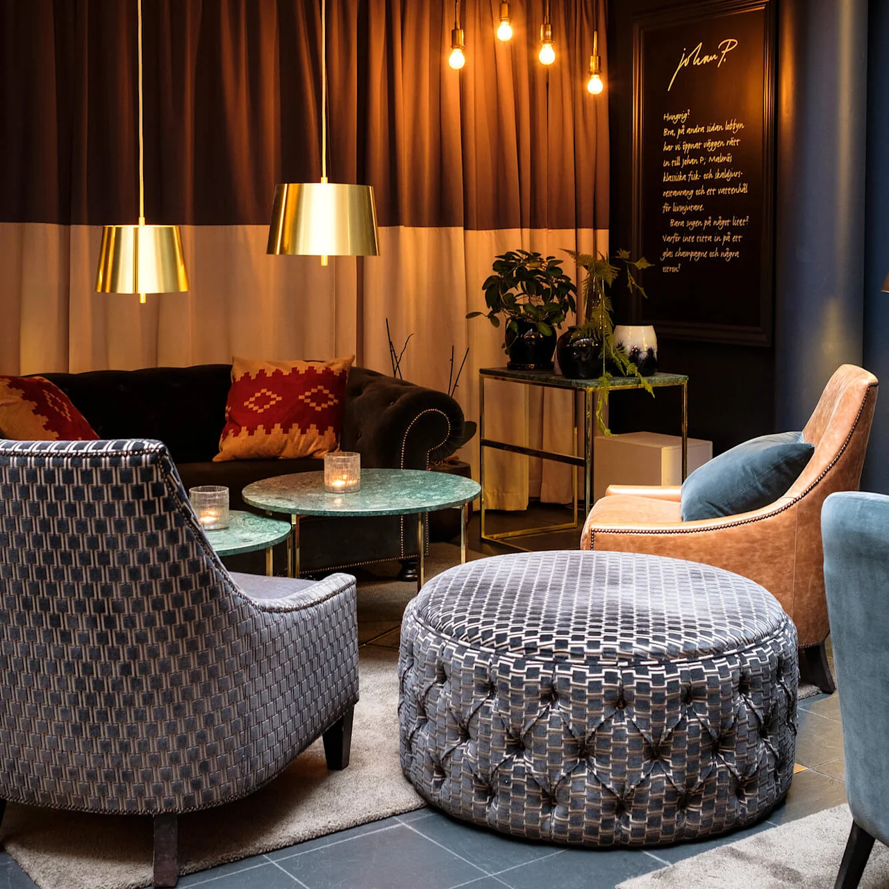 A cozy sitting area with eclectic armchairs, pendant lamps, bookshelves, and marble tables, evoking a warm atmosphere.