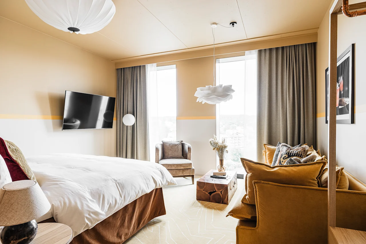 Et stilfuldt hotelværelse på Hernö Gin Hotel med en stor seng, en hyggelig sofa og lyse vinduer, designet til afslapning.