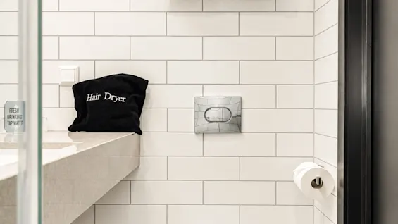 Modern hotel bathroom with white subway tiles, toilet, towels, and a bag labeled Hair Dryer.