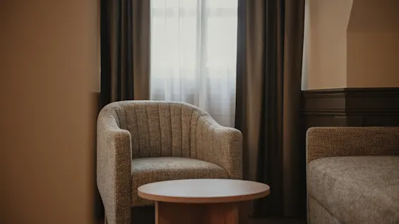 Et behageligt siddeområde med en lænestol, et lille bord og en sofa, badet i blødt lys fra et vindue.