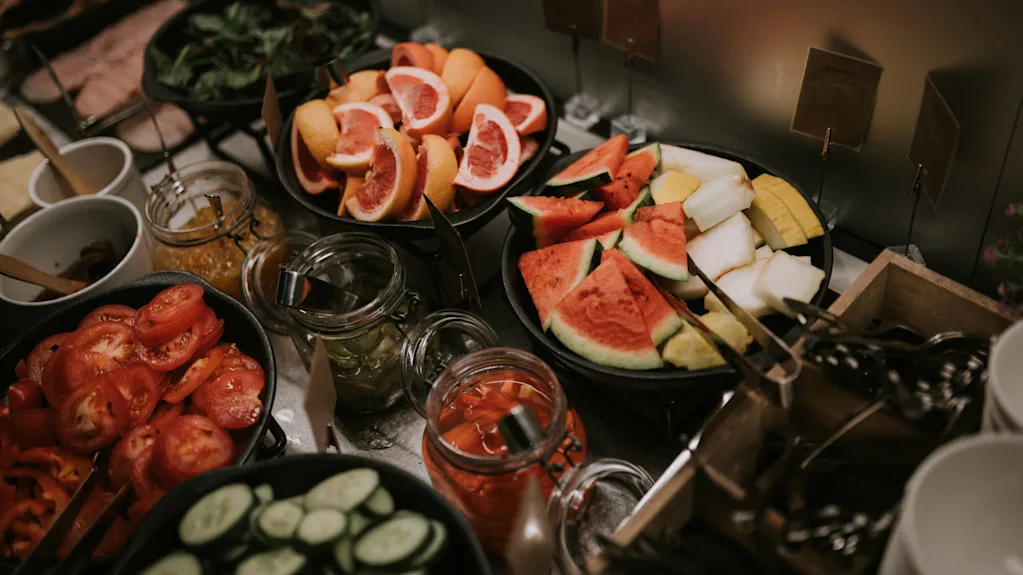 Forskellige friske frugter og grøntsager udstillet i skåle og krukker på et buffetbord.