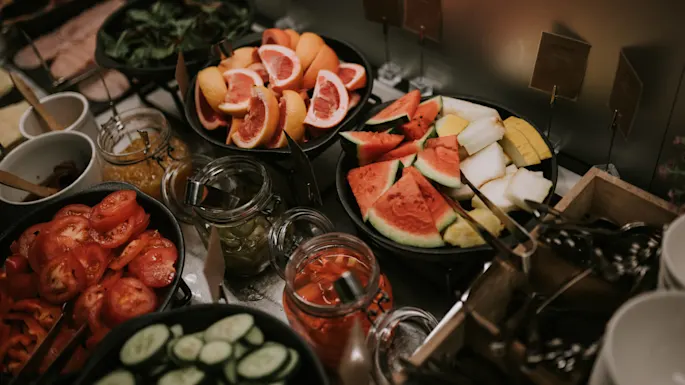 Ferske frukter og grønnsaker assortert i boller og krukker på et buffébord.