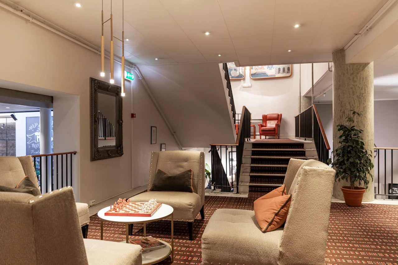 An inviting lounge area at Home Hotel Grand Bodø, featuring plush seating, a chessboard, and a grand staircase to another level.