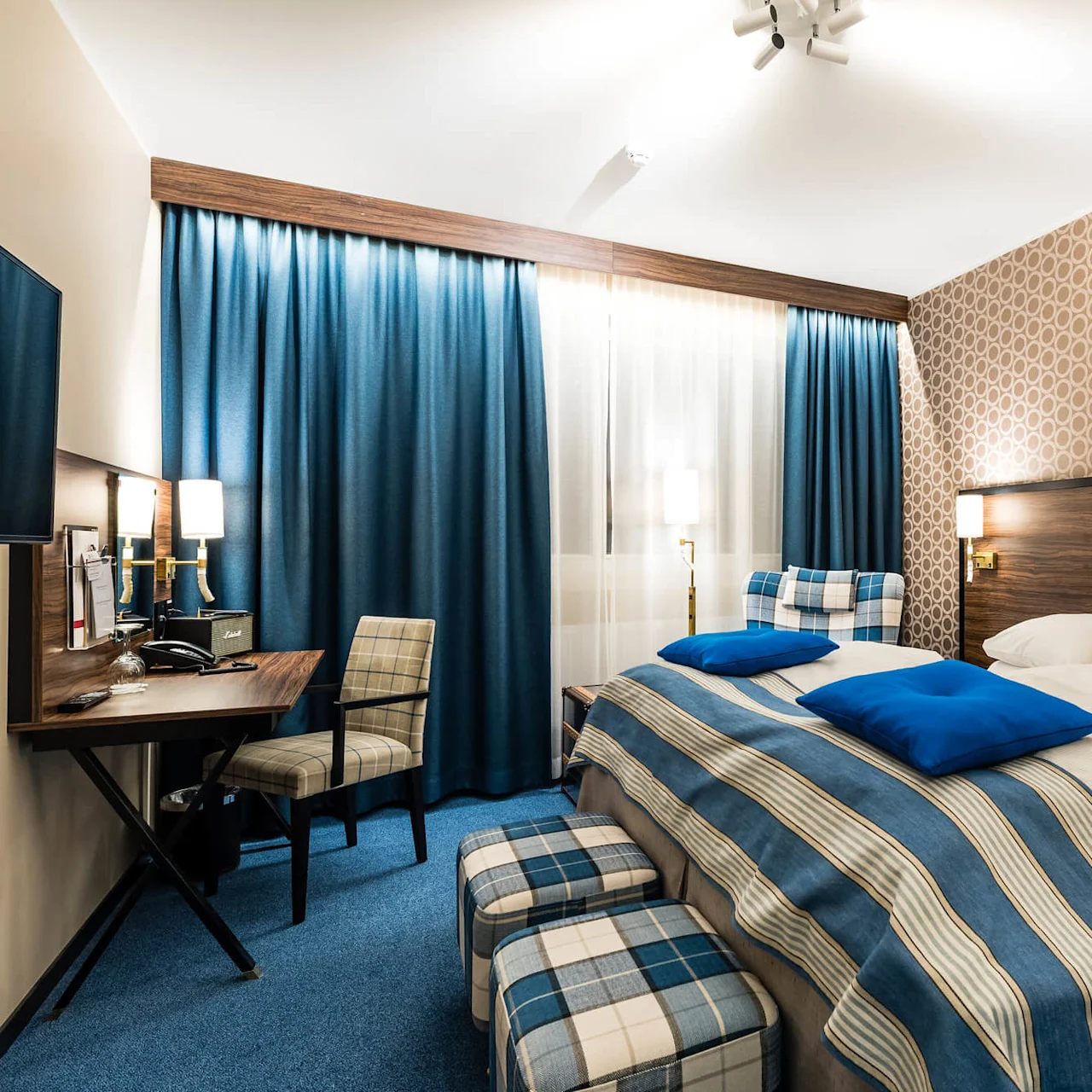 Ett snyggt ordnat hotellrum med blå accenter, mönstrad tapet och bäddad säng som antyder gästfrihet och komfort.