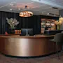 Et moderne hotellresepsjons- og barområde med en buet kobberdisk, barkrakker og hyller fylt med flasker.