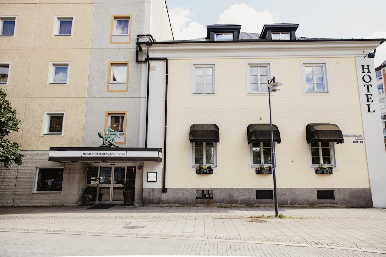 Eksteriør utsikt over en bygning med to arkitektoniske stiler, med et inngangsskilt som leser HOME HOTEL BERGMASTAREN og et vertikalt HOTEL-skilt.