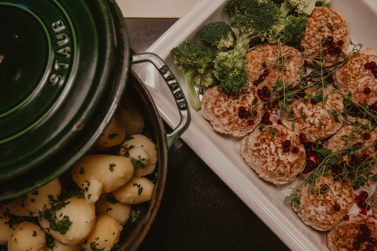 Et solidt måltid med en gryde urtekrydrede kartofler og et fad med velsmagende bøffer, frisk broccoli og røde bær.