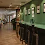 A stylish hotel hallway at Home Hotel Uppsala with a long green counter and bar stools, framed art on green walls, and lush plants.