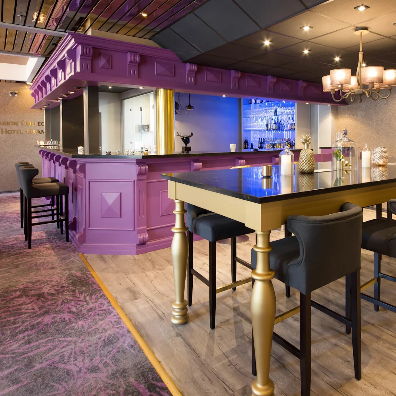 En chic bar med lila front, guldiga accenter, höga pallar och elegant belysning, inuti en modern lokal.