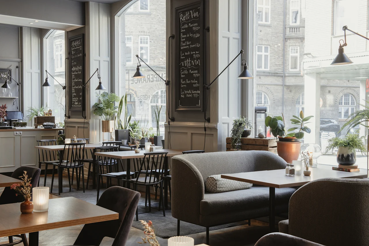 Et innbydende restaurantinteriør med ulike sitteplasser og store vinduer. Krittavler viser menyer for Rott Vin og vitt vin.