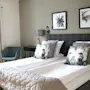 Ett mysigt hotellrum med en bäddad dubbelsäng, prydnadskuddar, tavlor på väggen och en fåtölj vid fönstret.