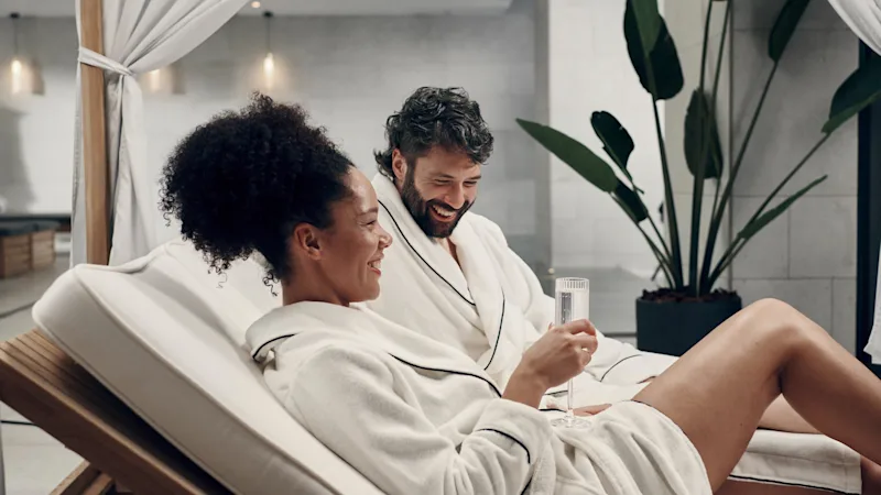 Wellness på Clarion Hotel. Kaksi kylpytakkiin pukeutunutta henkilöä rentoutuu ja hymyilee rauhallisessa kylpyläympäristössä.