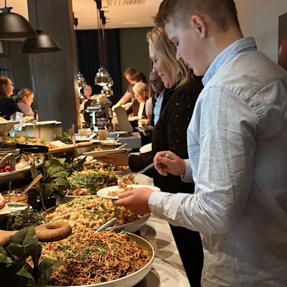 Folk forsyner seg fra en buffet med ulike retter, inkludert salater og pasta.