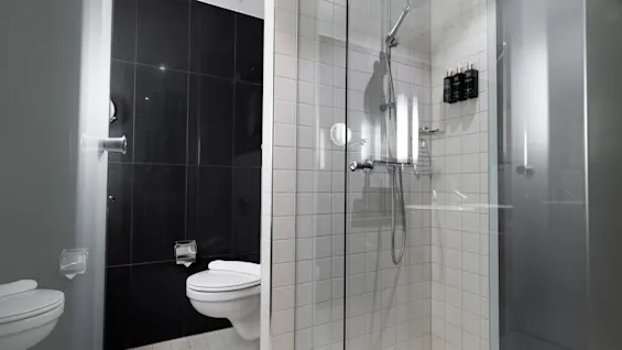 A modern bathroom with a wall-mounted toilet beside a glass-enclosed shower, featuring white and black tiled walls. No text is present.