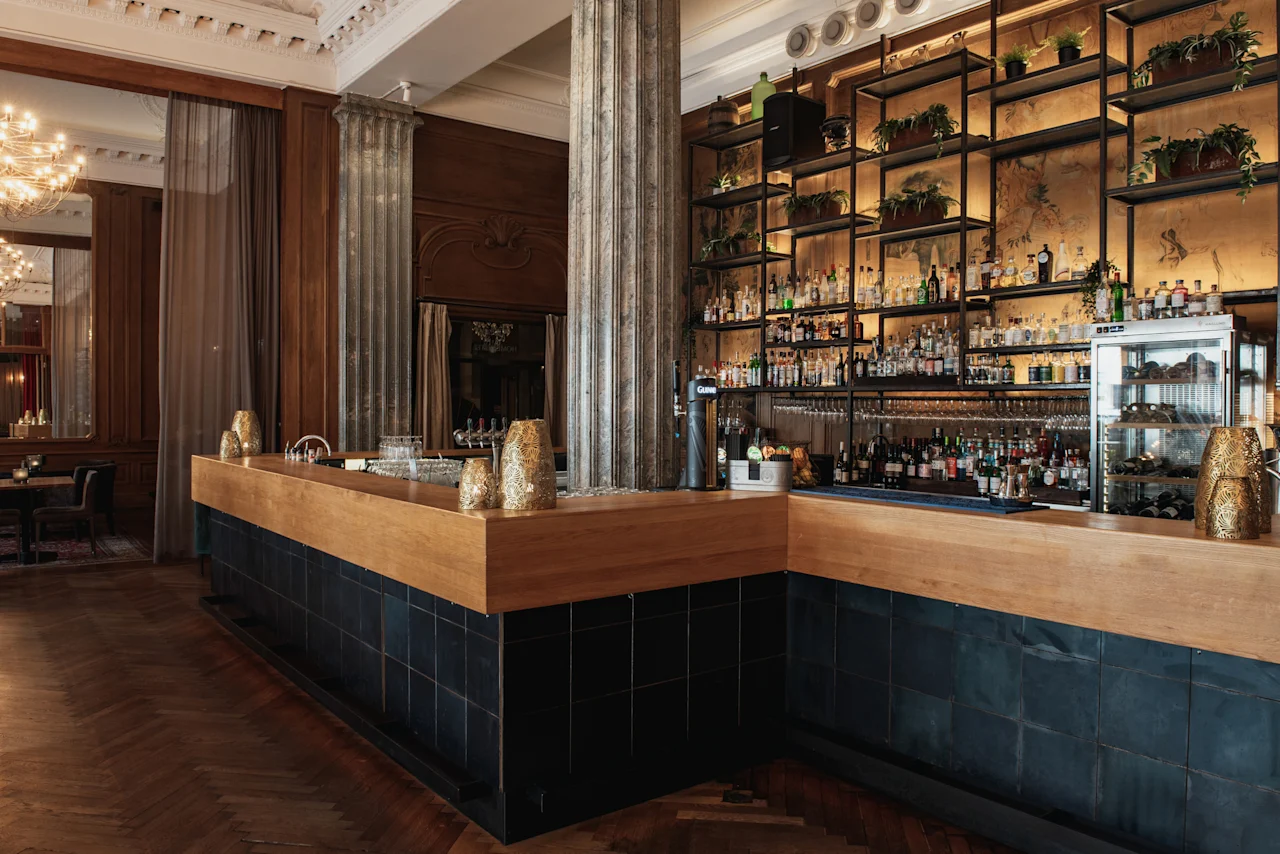 En stilfull bar på Home Hotel Grand, Helsingborg, med en lång trädisk och hyllor fyllda med flaskor och grönska.