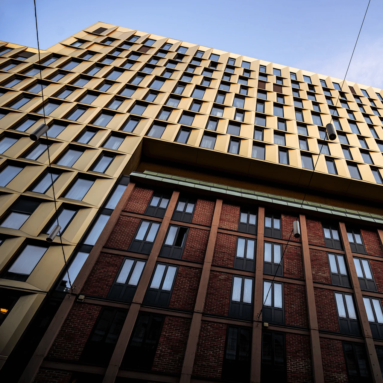 Tall modern building with golden and brick facade; viewed from below, wires cross overhead against a clear sky.