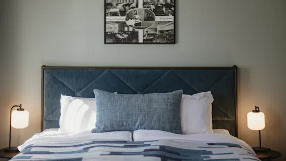 Ett hotellrum med en säng, blå sänggavel och lampor. Ovanför sängen finns en kollage med bilder och texten Oskarshamn Vastervik.