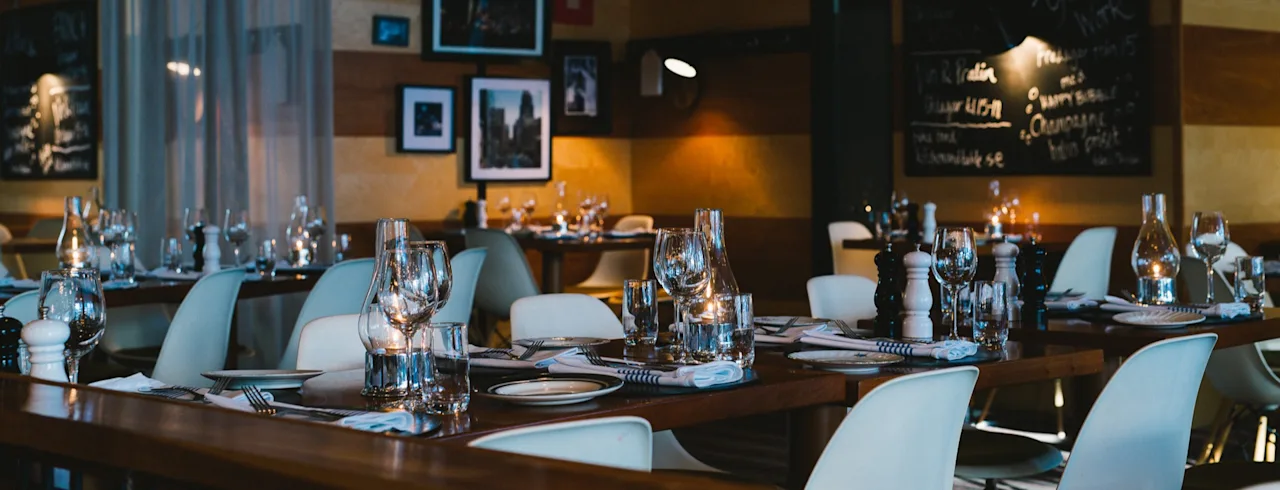 Et hyggeligt restaurantinteriør med borde dækket til spisning. En tavle annoncerer Brunch, After Work, Happy Bubble og Champagne.