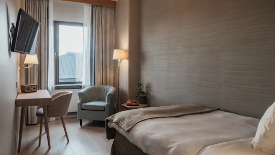 Et hyggeligt og funktionelt hotelværelse på Home Hotel Wellington, med en komfortabel seng, et skrivebordsområde og en afslappende lænestol ved vinduet.