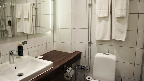 A modern bathroom with a sink, towel rack with two towels, and a shower area reflected in a mirror.