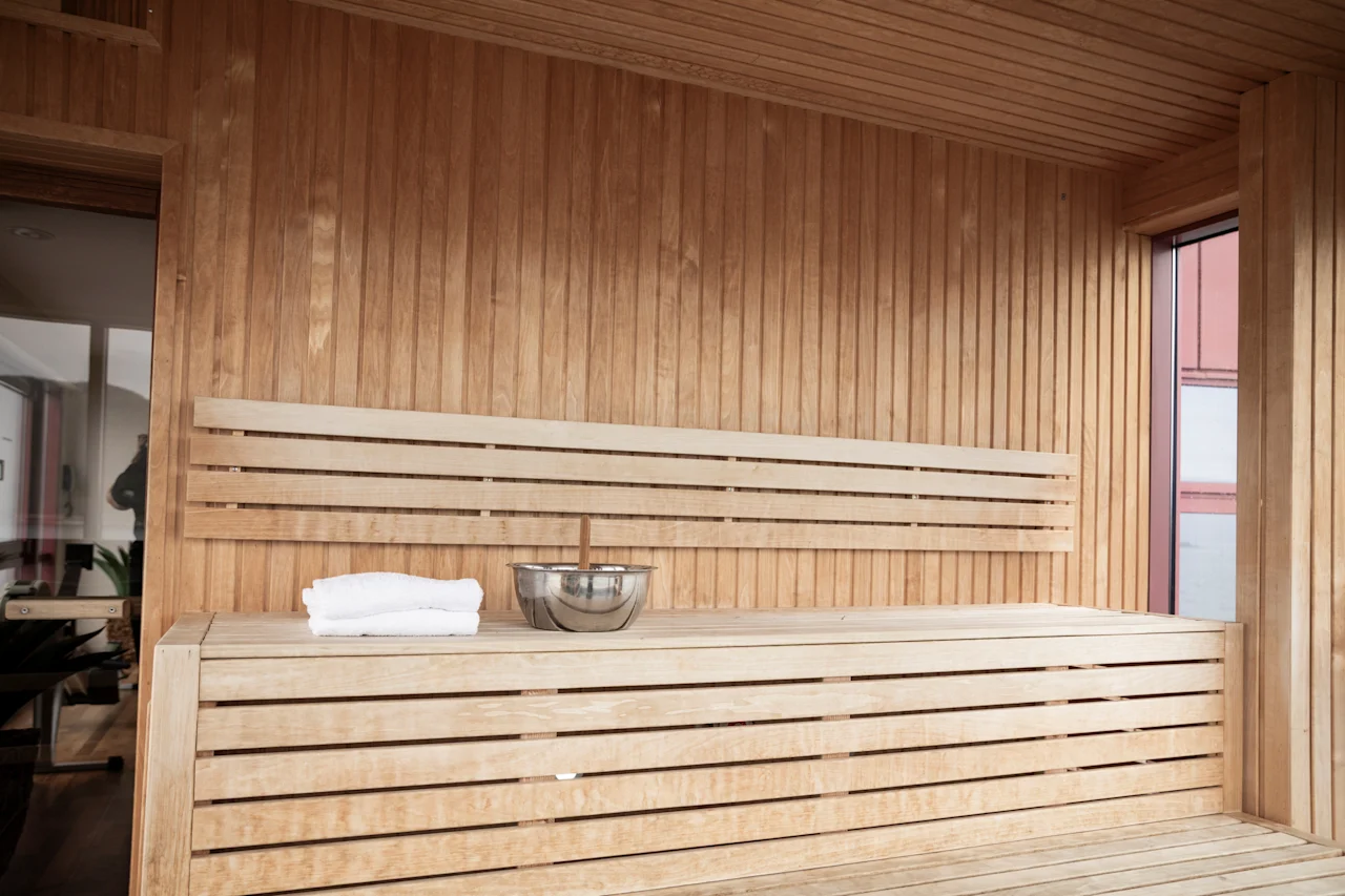 Rauhallinen saunahuone, jossa on vaaleat puupenkit ja seinät, kulho ja pyyhe valmiina virkistävään istuntoon.