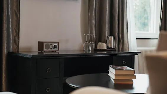 A welcoming room with a desk holding a radio and refreshment items, and books on a coffee table, perfect for relaxation.