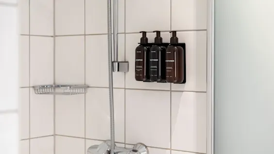 A shower with white tiles and dispensers for SHAMPOO, BODY WASH, and CONDITIONER, ready for use.
