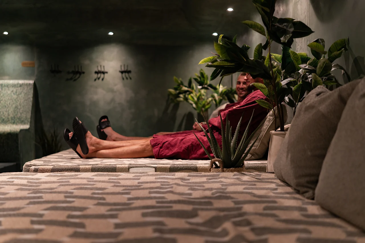 Henkilö nauttimassa rentoutumishetkestä mukavassa ympäristössä, yllään punainen kylpytakki, rehevän kasvillisuuden ympäröimänä.