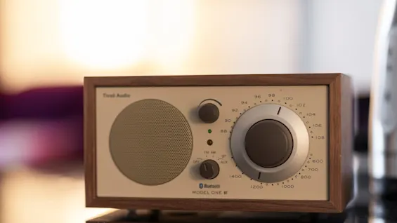 Lähikuva retrotyylisestä radiosta puukehyksellä, jossa on valitsimet FM AM:lle, AUX:lle ja Bluetoothille. MODEL ONE näkyy.
