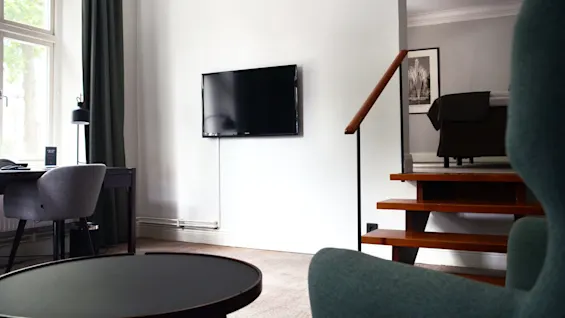 Et moderne stueområde med en flatskjerm-TV montert på veggen, minimalistiske møbler og en tretrapp til høyre.