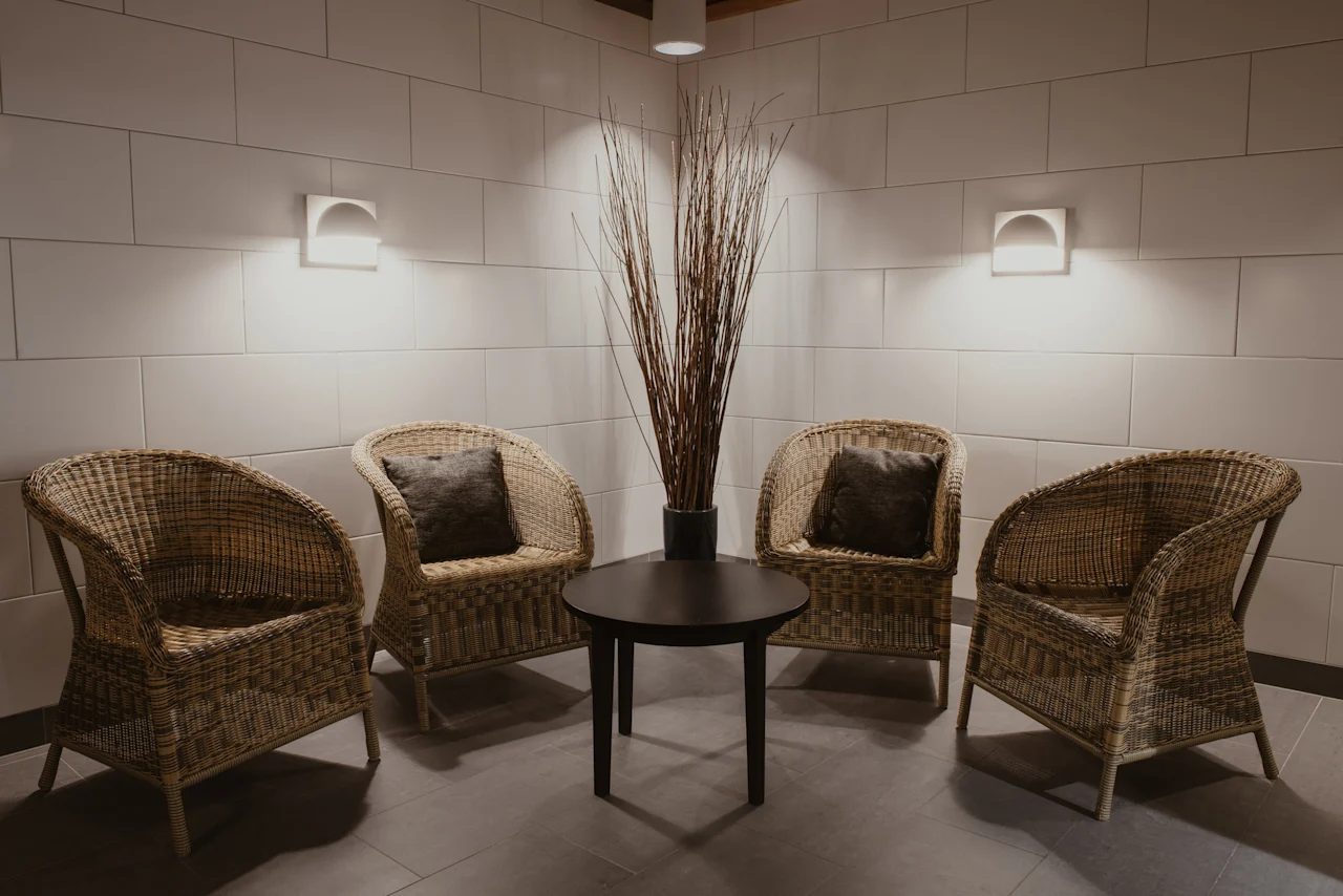 En mysig väntplats med fyra rottingstolar runt ett litet bord, upplyst av mjuka vägglampor.