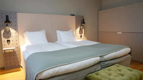 Viihtyisä hotellihuone, jossa mukava sänky, kaksi lukuvaloa ja vihreä rahi, täydellinen rentouttavaan oleskeluun.