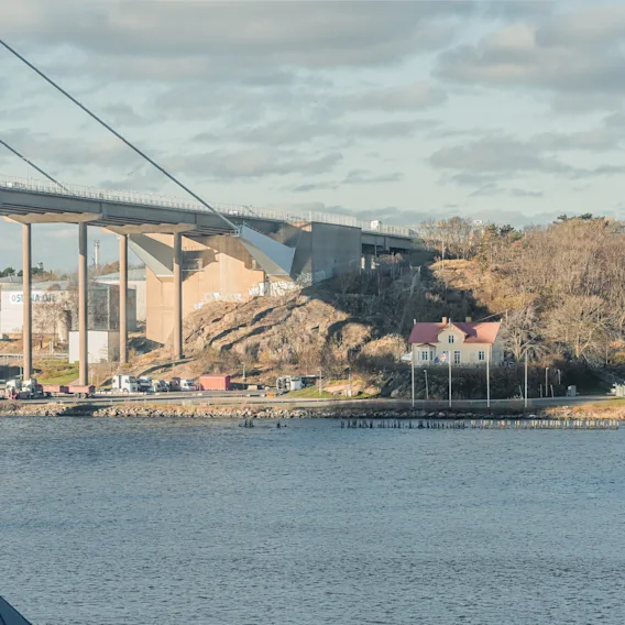 En naturskön vy av en stor bro över vatten, ansluten till en trädtäckt landmassa med byggnader under molnig himmel.