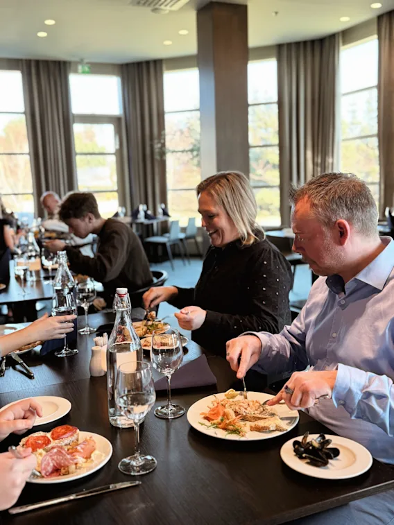 Folk som nyter et måltid sammen på en restaurant, med store vinduer som slipper inn naturlig lys.