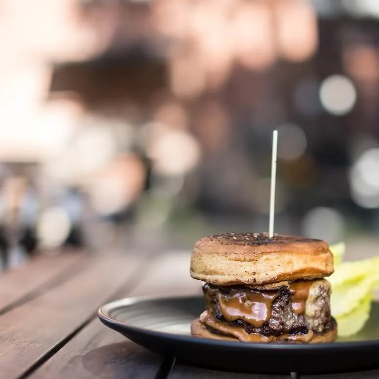 A juicy burger on a plate, skewered with a toothpick, on a wooden table, outdoors.