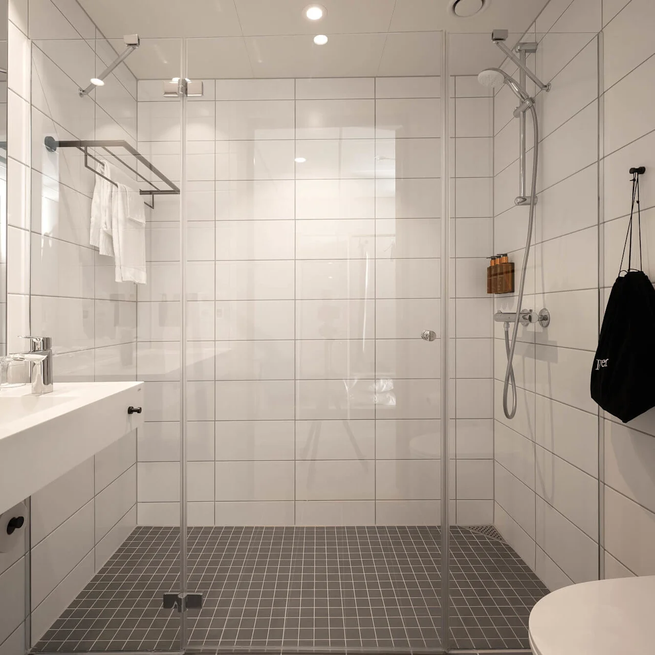 Et moderne badeværelse med walk-in bruser, hvid forfængelighed, og spejlet skab, der udstråler renlighed og minimalisme.