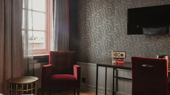 Ett mysigt hotellrum på Home Hotel Grand, Helsingborg, med en bekväm röd fåtölj, skrivbord och TV för avkoppling.