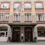 En fleretagers bygning med murstens- og stenfacade, med en fremtrædende indgang med markise og et flag, der viser HOME HOTEL.
