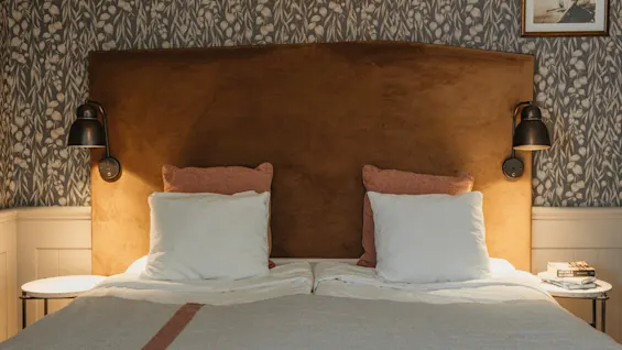 An inviting bedroom featuring a bed with a brown headboard, soft pillows, and warm lighting from two wall-mounted lamps.