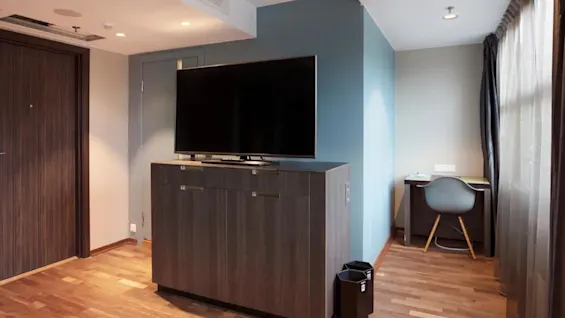 Television on a wooden cabinet, placed against a blue wall in a modern room. A small desk with a chair is in the corner, near a window with curtains.