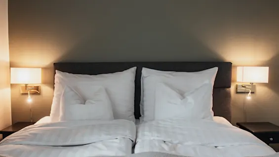 En koselig hotellseng på Home Hotel Norre Park i Halmstad, med mykt hvitt sengetøy og varm belysning fra nattbordslamper.